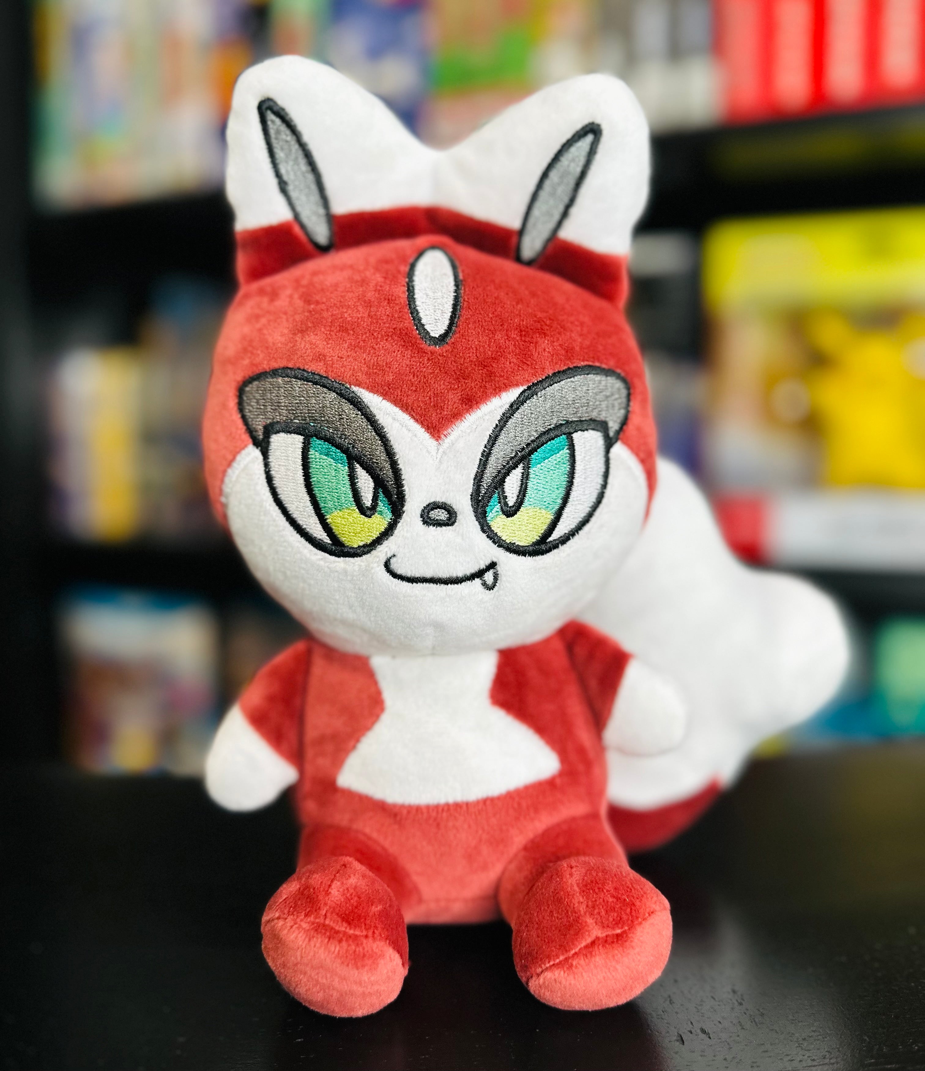 Front view of the Folkachi plush from Histrobea Chronicles, featuring its red and white fur, large green eyes, and fox-like design. A collectible plush toy associated with the HoopsandHipHop YouTube channel.