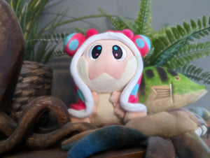 Snugooi plush from Lockstin & Gnoggin's Lockemon series, featuring a cute sea slug design with blue and pink accents. Posed in a natural setting with plants and ocean-themed decor, perfect for plush collectors and fans of the Lockemon series.