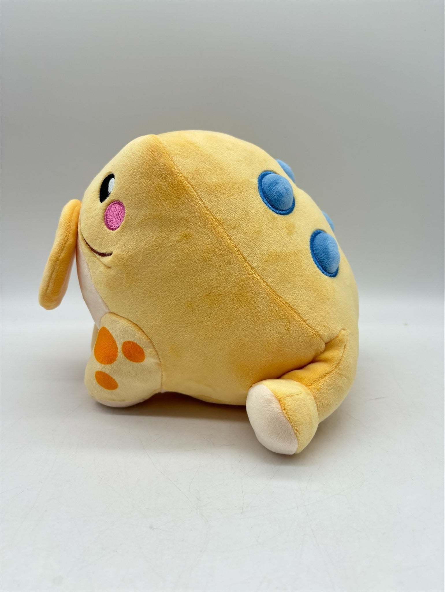 Side view of TOTYM's Jin Chan frog plush, showing soft beige fabric with orange spots on the legs and blue circular accents on the back. Kawaii mythical creature design ideal for collectors.